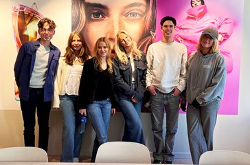 Group of students smiling in front of a larger artwork at an H&M office