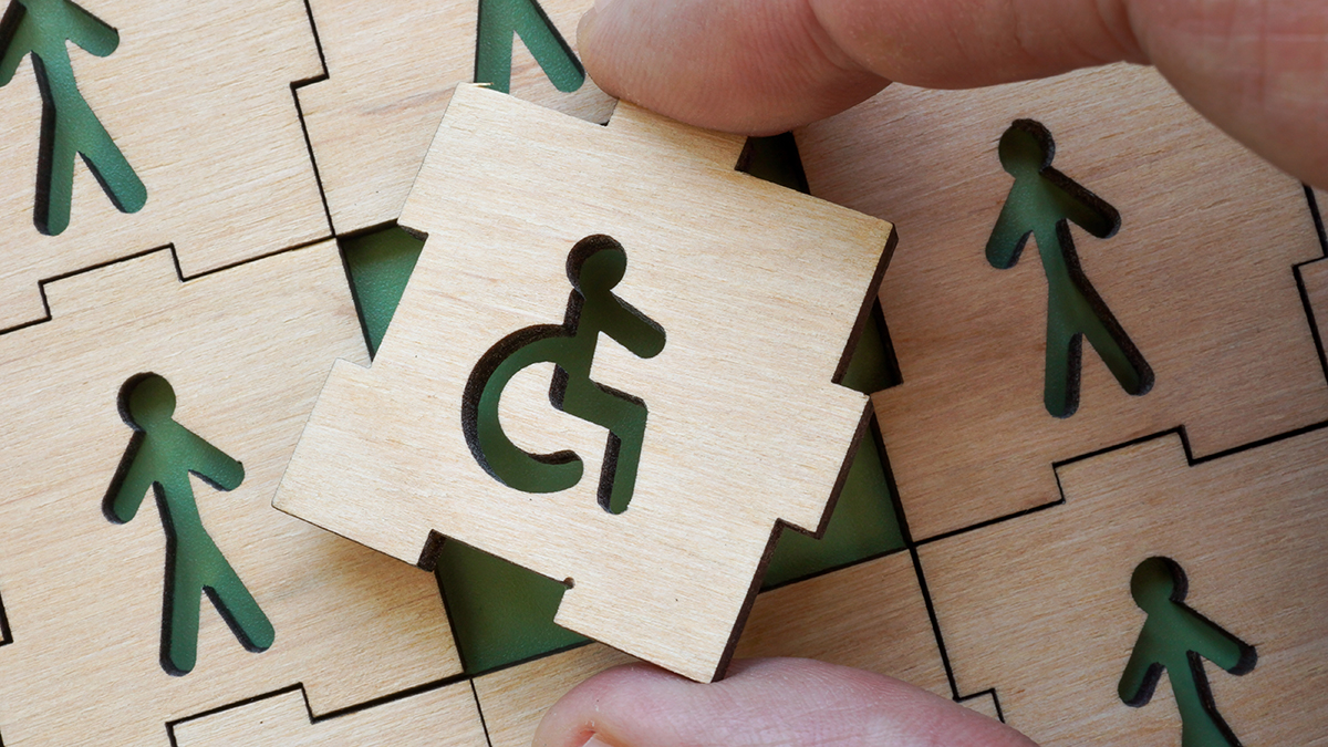 Hand holding puzzle piece with disability symbol. Concept of inclusion in work and society.